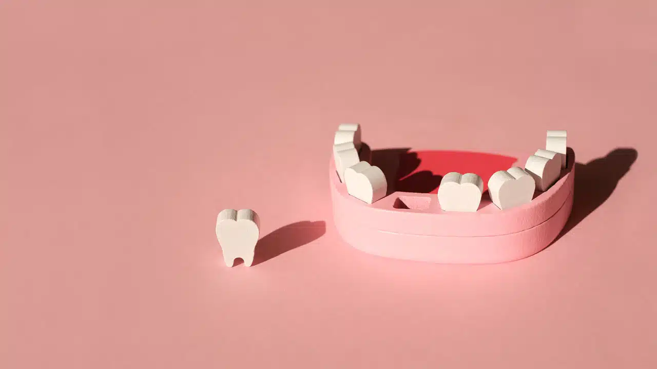 Wooden model toy of a human jaw with a missing tooth on a pink studio background