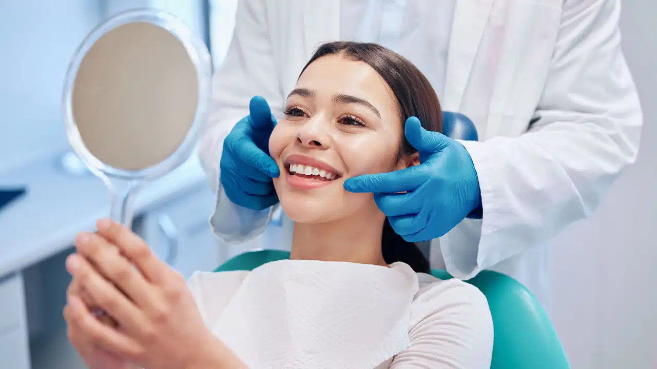 Woman looking at teeth in dental mirror after oral surgery